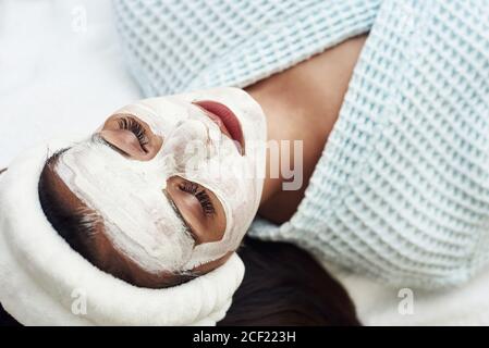 Spa-Konzept. Junge Frau mit Nährstoff Gesichtsmaske im Schönheitssalon, Nahaufnahme. Die Kosmetikerin trägt eine feuchtigkeitsspendende Maske auf das Gesicht des Kunden auf. Stockfoto