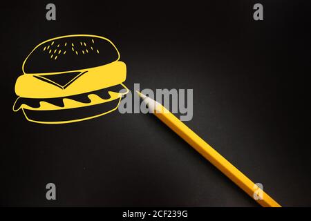Hamburger Icon-ähnliche Zeichnung in gelbem Fast Food auf schwarzem Brett mit gelbem Bleistift dazu. Fatfood ungesunde Ernährung Konzept Stockfoto