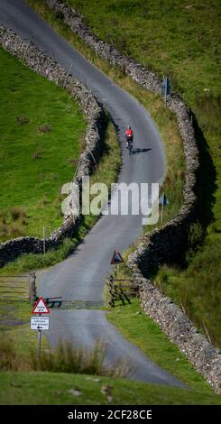 Die Radfahrerin klettert mit ihrem Elektrofahrrad einen steilen Hügel im Yorkshire Dales Nationalpark, Großbritannien. Stockfoto