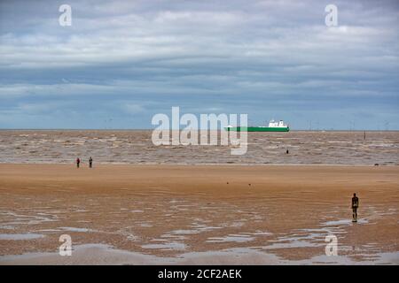 Ein Tankschiff auf dem Fluss Mersey, während die Leute am Strand von Crosby, Sefton in Merseyside entlang laufen. Stockfoto