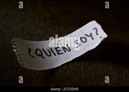 Ein Stück Papier mit der Frage wer bin ich geschrieben in Spanisch, auf einer schwarzen strukturierten Oberfläche Stockfoto