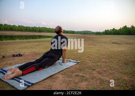 Mann, der Surya namaskar im Wald bei Morgendämmerung durchführt Stockfoto