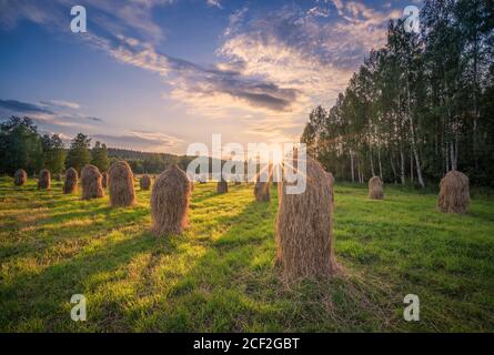 Altmodische Heuhaufen mit wunderschönen goldenen Sonnenuntergängen und Sonnenlicht Warmer Sommerabend in Finnland Stockfoto