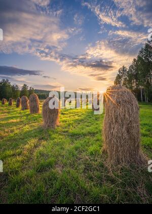 Altmodische Heuhaufen mit wunderschönen goldenen Sonnenuntergängen und Sonnenlicht Warmer Sommerabend in Finnland Stockfoto