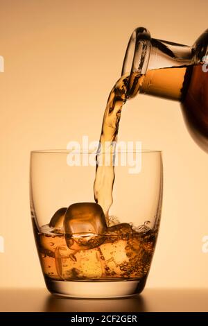 Gießen Whiskey oder anderen Alkohol in ein Glas mit Eis. Close-up vertikale Foto, oranger Hintergrund Stockfoto