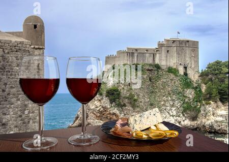 Zwei Gläser Wein mit Blick auf die Festung Lovrijenac von Dubrovnik Stadtmauer, Dubrovnik, Kroatien. Ein Glas Rotwein mit verschiedenen Snacks - Teller wi Stockfoto