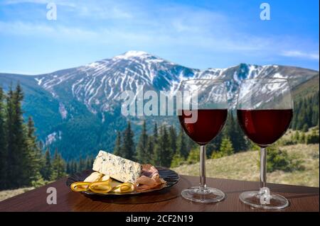 Zwei Gläser Wein mit Käse- und Fleischsortiment mit Blick auf die Berglandschaft. Glas Rotwein mit verschiedenen Snacks - Teller mit Schinken, in Scheiben geschnitten, Stockfoto