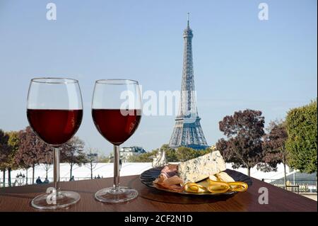 Zwei Gläser Rotwein mit Snacks mit Blick auf Paris und den Eiffelturm. Glas Rotwein mit verschiedenen Snacks - Teller mit Schinken, in Scheiben geschnitten Stockfoto