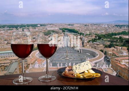Zwei Gläser Rotwein mit Käse- und Fleischauswahl vor dem Blick auf den Petersplatz im Vatikan, Rom, Italien. Skyline von Rom. Panoramablick Stockfoto