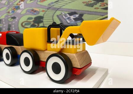 Gelb und rot Spielzeug Auto Bulldozer mit einem Eimer gemacht Aus Kunststoff und Holz steht auf einer weißen Oberfläche Stockfoto