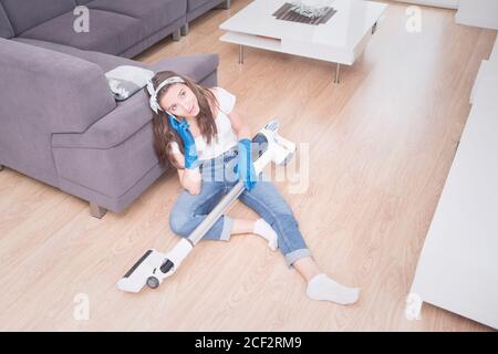 Junges Mädchen reinigt die Wohnung. Müde Mädchen nach der Reinigung sitzt auf dem Boden mit einem Staubsauger und spricht am Telefon. Stockfoto