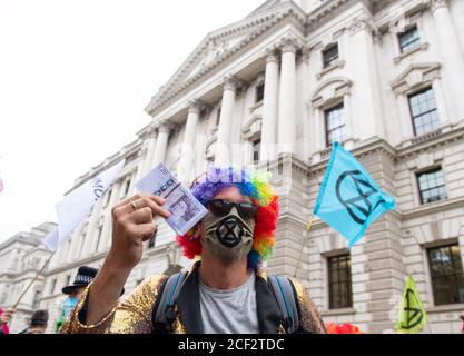 Ein als Clown gekleideter Protestler hält während eines Extinction Rebellion Protestes in Westminster, London, ein Bündel gefälschtes Geld vor dem HM Treasury Building. Die Umweltkampagnengruppe hat Veranstaltungen geplant, die an mehreren Sehenswürdigkeiten der Hauptstadt stattfinden sollen. Stockfoto