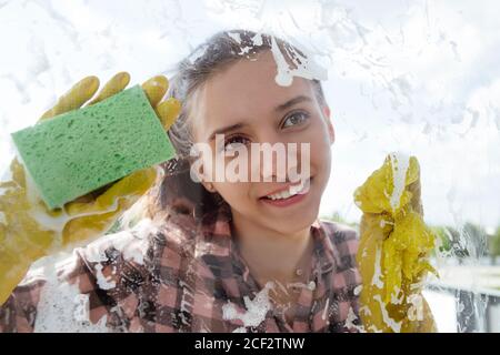 Reinigungshaus Concepta junges Mädchen mit einem Lächeln in gelben Gummihandschuhen wäscht ein Fenster von außen. Stockfoto