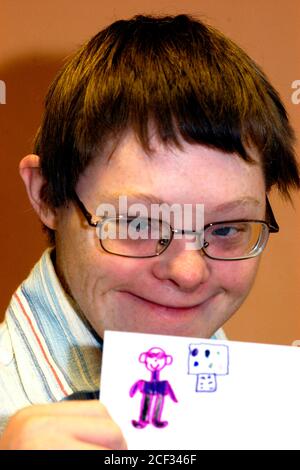Junger Mann mit Downs-Syndrom bei einer Unterstützungsgruppe für Menschen mit Lernbehinderungen halten sein Selbstporträt UK hoch Stockfoto