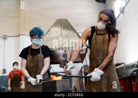 Schmiede in Masken schlagen heißes Metall mit Hammer während der Arbeit Stockfoto