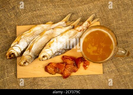 Getrockneter Fisch, getrockneter Kaviar und ein Bierkrug auf einem hölzernen Servierbrett. Nahaufnahme Stockfoto