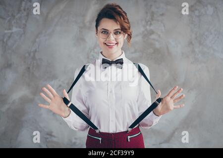 Portrait von ihr sie schön aussehende schöne schöne ziemlich fröhlich fröhlich Wellig-haarige Mädchen ziehen Hosenträger mit Spaß isoliert über grauen Beton Stockfoto