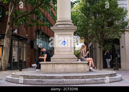 Leute, die an der Sonnenuhr von Seven Dials sitzen, Touristen- und Einkaufsviertel in Covent Garden, London, England, Großbritannien Stockfoto