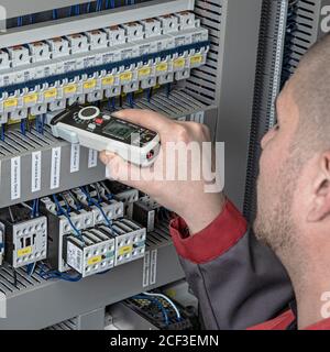 Elektriker, der mit einem Strommessmultimeter in einem Schaltschrank misst Stockfoto