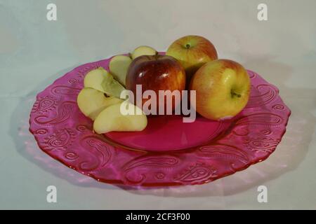 Äpfel ganz und geschnitten, präsentiert auf einem schönen rosa Glasplatte Stockfoto