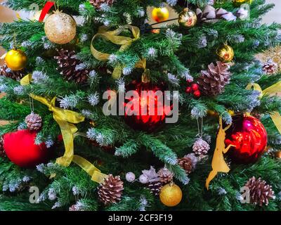 Der Weihnachtsbaum ist mit roten und goldenen Kugeln, Bändern und Tannenzapfen geschmückt. Nahaufnahme Stockfoto