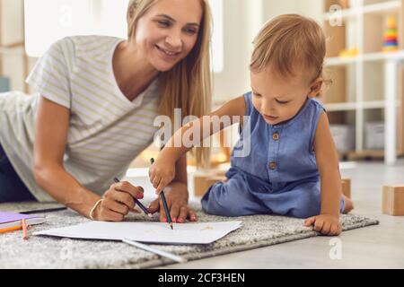Liebenswert Kleinkind Kritzelei auf Papier mit Bleistift, während sitzend auf Boden mit seinem jungen Kindermädchen Stockfoto