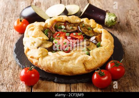 Pikante Auberginen-Galette-Torte mit Tomaten, Zwiebeln und Kräutern aus der Nähe auf einem Schieferbrett auf dem Tisch. Horizontal Stockfoto