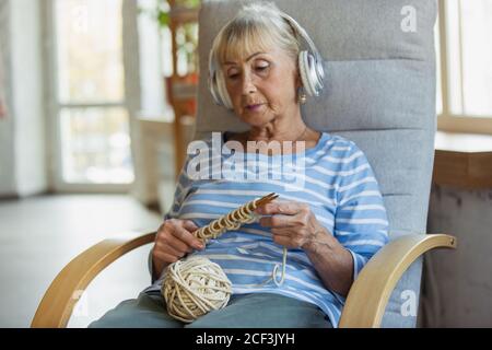 Lernen, mit einem Online-Dozent zu stricken. Ältere Frau, die zu Hause studiert, Online-Kurse bekommt, Selbstentwicklung. Kaukasische Frau mit modernen Geräten für die Bildung, verbringen Zeit für neue Arbeit oder Hobby. Stockfoto