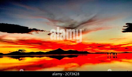 Dramatischer roter Sonnenuntergang über Salar de Uyuni, Wüste Atacama. Altiplano Plateau, Bolivien, Südamerika. Magische Himmelsreflexion im Wasser des Sees. Stockfoto