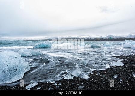 Wellen krachen lange Belichtungsbewegung auf blauem Gletscher Eisberg Eis Schwimmend auf schwarzem Sand am Jokulsaron Lagune See Diamant Strand In Island Stockfoto