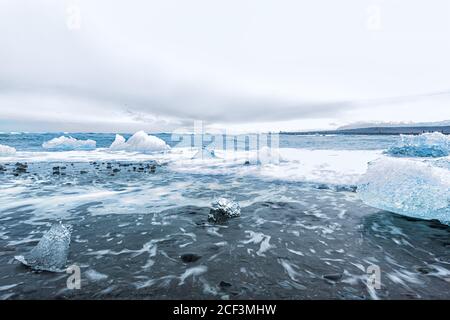 Wellen Shore lange Belichtungsbewegung auf blauem Gletscher Eisberg Eis Schwimmend auf schwarzem Sand am Jokulsaron Lagune See Diamant Strand In Island Stockfoto