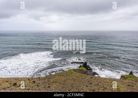Island Landschaft Blick von Südosten Ring Road Reise braun felsig Bergklippe am bewölkten Tag mit Atlantik und Wellen Absturz Stockfoto