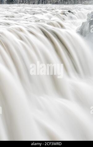 Isländischer Dettifoss Wasserfall vertikal in isländischem Grau Langzeitbelichtung glatt Wasser in Bewegung und Felsklippen sprühen Stockfoto