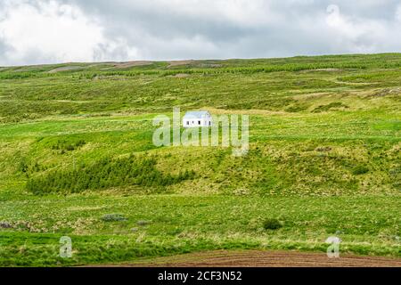 Landschaftsansicht von Island Wiese grün Gras Hügel offenen Feld In der Nähe Skutustadagigar und See Myvatn während bewölkten Tag und klein Haus im Sommer Stockfoto