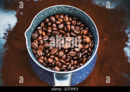 Auf dem gemahlenen Kaffee ist ein schöner blauer Cezve, der mit gerösteten Kaffeebohnen gefüllt ist, die dann starken Kaffee gemacht werden. Stockfoto