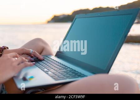 Eine Frau arbeitet ferngesteuert auf einem Laptop. Nahaufnahme der Hände. Meer im Hintergrund. Das Konzept des Freelancens und Bloggens. Stockfoto