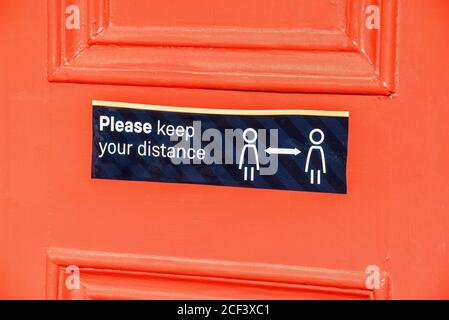 Hampshire, England, Großbritannien. 2020. Ein Halten Sie Ihre Entfernung Zeichen auf einer orangefarbenen Tür während Covid-19 Ausbruch. Stockfoto