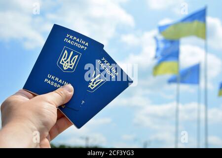 Neuer ukrainischer blauer biometrischer Pass mit Identifikations-Chip auf gegen blauen Himmel und winkende Flagge Hintergrund. Stockfoto