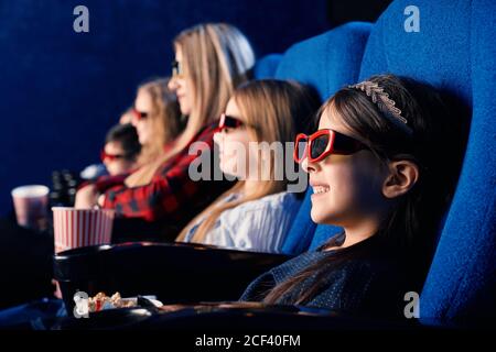 Selektiver Fokus von lachendem Kind trägt 3d-Brille, essen Popcorn und sehen lustige Filme. Nettes kleines Mädchen genießen Zeit mit Freunden im Kino. Konzept der Freizeit und Unterhaltung. Stockfoto