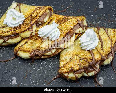 Crepes mit Bananenscheiben und Schokolade auf Schiefer serviert Stockfoto