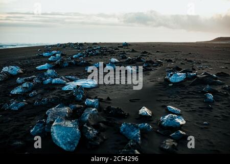 Raue Felsen an der sandigen Küste in der Nähe von Meer gegen bewölkt Morgenhimmel in der Natur Stockfoto