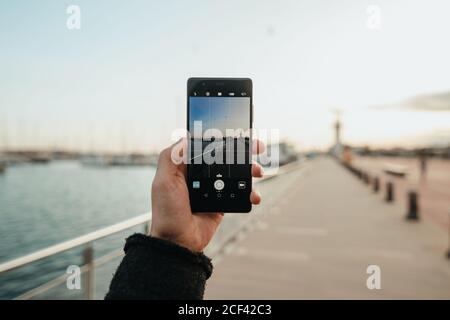 Hand von anonymen Mann mit Smartphone zu fotografieren Leerer Damm am Abend Stockfoto