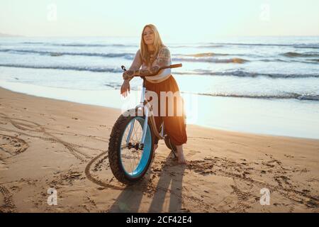 Fröhliche Frau, die am ruhigen Strand mit dem Fahrrad unterwegs ist Stockfoto