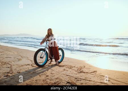 Fröhliche Frau, die am ruhigen Strand mit dem Fahrrad unterwegs ist Stockfoto
