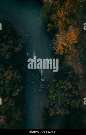 Von oben schaumig dunkler Fluss, der zwischen Bäumen mit Grün fließt Orangefarbenes Laub Stockfoto