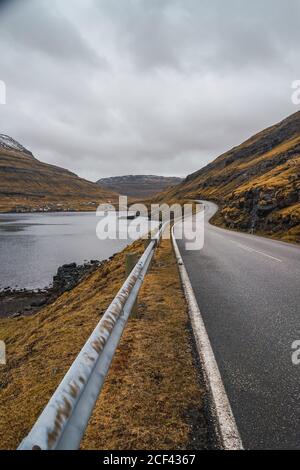 Kurvige Asphaltstraße durch hügeliges Gelände am bewölkten Tag Auf den Färöern Stockfoto