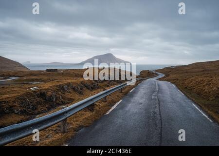 Kurvige Asphaltstraße durch hügeliges Gelände am bewölkten Tag Auf den Färöern Stockfoto