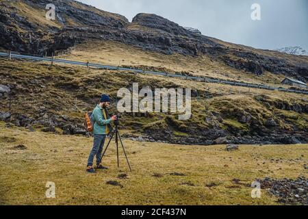 Bärtiger Mann in Winterkleidung mit einer Fotokamera Ein Stativ im Freien in Färöer-Inseln Landschaft Stockfoto