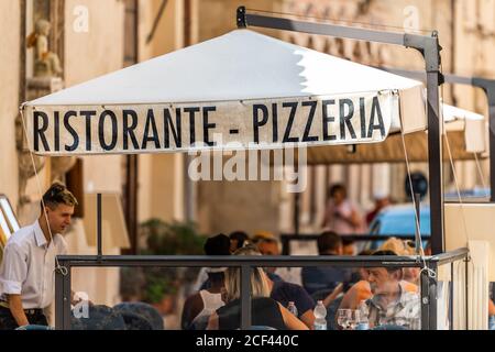 Assisi, Italien - 29. August 2018: Stadt in Umbrien während des Sommertages mit Restaurant Pizzeria Schild und Menschen sitzen im Urlaub Essen Stockfoto