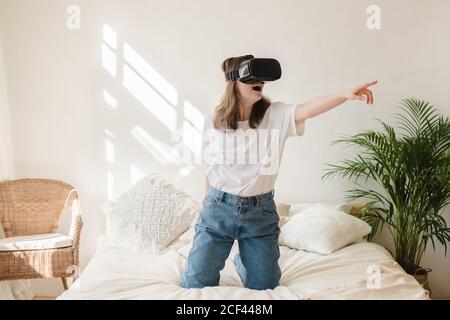 Junge Frau in Jeans und weißem T-Shirt mit Virtual Reality Brille auf dem Kopf bewegt ihre Arme, tanzt, bekommt Angst. Das Konzept der modernen Technologie, Stockfoto